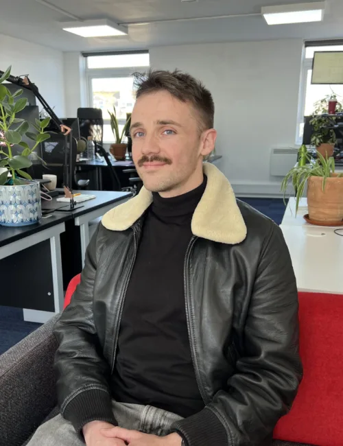 Person in black leather jacket sitting on a sofa in an office